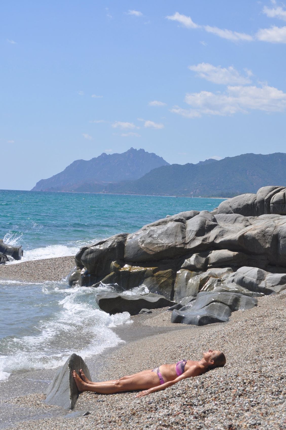 Frau, die am Meer auf den Kieseln liegt — Sardinien
